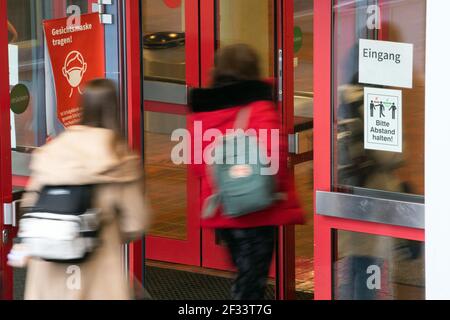 Bergisch Gladbach, Germania. 15 marzo 2021. Gli allievi della Städtische Integrierte Gesamtschule Paffrath camminano attraverso l'ingresso della scuola, sulle cui finestre sono presenti avvisi che indicano che le maschere sono obbligatorie e che si applicano le regole di distanza. Nonostante l'aumento delle infezioni, tutti gli alunni della Renania Settentrionale-Vestfalia devono tornare nelle loro aule, almeno per un giorno. A Bergisch-Gladbach, la distribuzione di test di spit agli alunni inizia un giorno prima delle altre scuole. Credit: Federico Gambarini/dpa/Alamy Live News Foto Stock