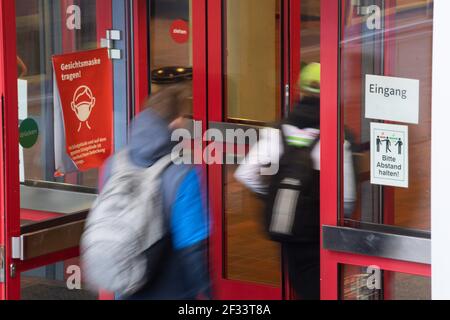 Bergisch Gladbach, Germania. 15 marzo 2021. Gli studenti della Paffrath Municipal Integrated Comprehensive School camminano attraverso l'ingresso della scuola, con avvisi attaccati alle finestre che indicano che le maschere sono obbligatorie e che si applicano le regole della distanza. Nonostante l'aumento delle infezioni, tutti gli alunni della Renania Settentrionale-Vestfalia devono tornare nelle loro aule, almeno per un giorno. A Bergisch-Gladbach, la distribuzione di test di spit agli alunni inizia un giorno prima delle altre scuole. Credit: Federico Gambarini/dpa/Alamy Live News Foto Stock