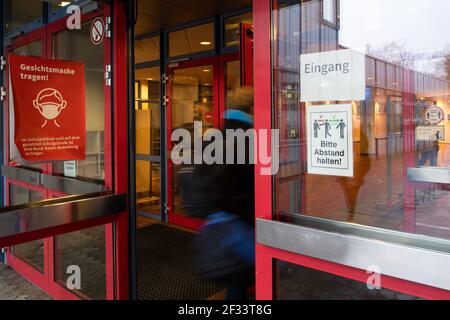 Bergisch Gladbach, Germania. 15 marzo 2021. Gli studenti della Paffrath Municipal Integrated Comprehensive School camminano attraverso l'ingresso della scuola, con avvisi attaccati alle finestre che indicano che le maschere sono obbligatorie e che si applicano le regole della distanza. Nonostante l'aumento delle infezioni, tutti gli alunni della Renania Settentrionale-Vestfalia devono tornare nelle loro aule, almeno per un giorno. A Bergisch-Gladbach, la distribuzione di test di spit agli alunni inizia un giorno prima delle altre scuole. Credit: Federico Gambarini/dpa/Alamy Live News Foto Stock