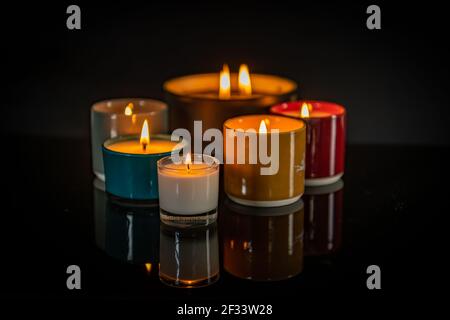 Candele profumate illuminate e riflettenti su una superficie nera lucida Foto Stock