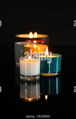 Candele profumate illuminate e riflettenti su una superficie nera lucida Foto Stock