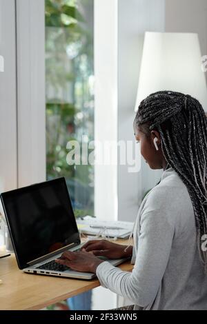 Una giovane studentessa universitaria piuttosto giovane che lavora su un computer portatile scrivania a casa Foto Stock