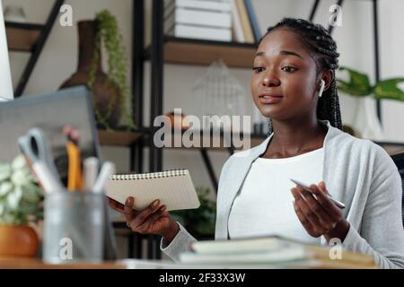Bella giovane donna nera con notebook in mano avendo online incontro con il cliente o il collaboratore e discussione del progetto Foto Stock