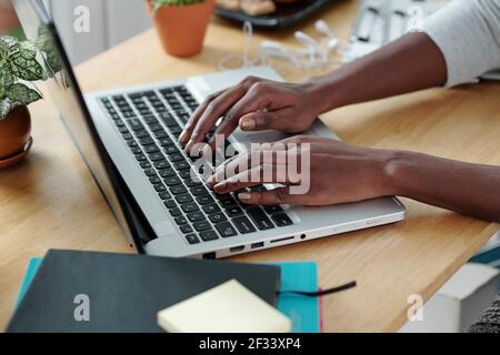 Mani di giovane donna che scrivano sul computer portatile quando si lavora a. scrivania da ufficio a casa Foto Stock