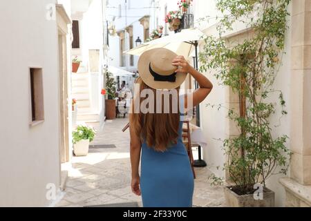 Vista posteriore di giovane donna turistica sulla strada antica della città vecchia. Donna di viaggio in cappello di paglia e abito blu godendo la vacanza in Italia. Turismo e trave Foto Stock