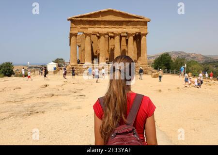 Giovane donna guarda al Tempio Concordia nella Valle dei Templi di Agrigento e la Sicilia. Traveler ragazza visite templi greci in Italia Meridionale in precedenza Foto Stock