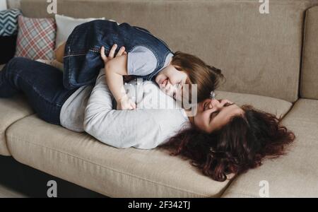 la ragazza felice piccola abbraccia la sua mamma mentre si sdraia a casa sul lettino Foto Stock