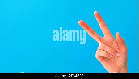 Primo piano di bella mano femminile facendo segno di vittoria, isolato su sfondo blu studio con spazio di copia per avversari. Concetto di linguaggio del corpo. Mano Foto Stock