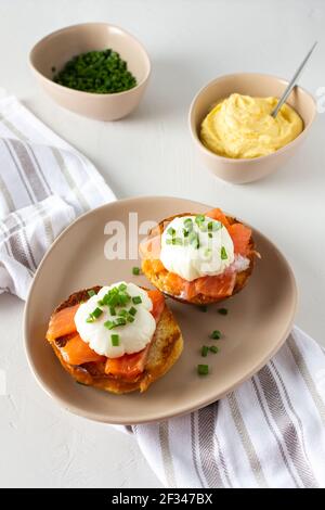 Deliziosa e abbondante colazione, uova dell'Atlantico in un piatto su sfondo bianco, panino fritto rotondo con salmone e uova Benedetto, salsa hollandaise Foto Stock