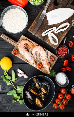 Paella spagnola cruda ingredienti con gamberi, seppie, cozze ed erbe su tavolo di legno nero, vista dall'alto, foto del cibo. Foto Stock