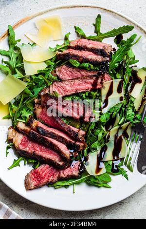 Bistecca di manzo tagliata con rucola e parmigiano su un piatto grigio, fondo grigio. Concetto di cucina Italiana. Foto Stock