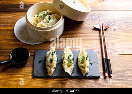 Gnocchi asiatici su ardesia di pietra e in legno a vapore sopra tavolo tradizionale in legno con salsa di soia e trissini e fresco vista laterale sulle erbe Foto Stock