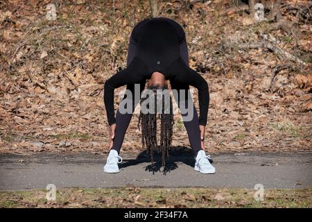 Una donna agile e flessibile negli anni cinquanta conduce una lezione di yoga meditativa quotidiana in un parco a Queens, New York City. Foto Stock
