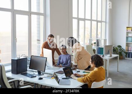 Visualizzazione ad alto angolo in diversi team di sviluppatori software che utilizzano computer in un ufficio moderno, con particolare attenzione ai project manager che sovrintende alla produzione, ai copy Foto Stock