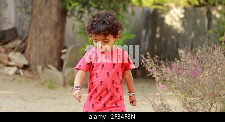 Un bambino di origine indiana che indossa una camicia rossa guardando verso il basso a terra, india.Concept per le gioie dell'infanzia, i ricordi dell'infanzia, il viso del bambino espelle Foto Stock