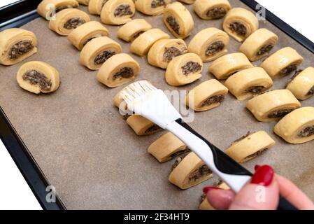 Una donna applica l'olio alle torte fresche di lievito crudo con funghi all'interno utilizzando una cazzuola da cucina in silicone. Foto Stock