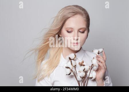 Giovane donna graziosa che tiene i fiori secchi di cotone su sfondo bianco Foto Stock