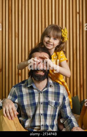 Piccola figlia e padre hanno divertimento a casa, faccia i volti divertenti facendo con le dita eyewear forma come occhiali guardando la macchina fotografica attraverso binocoli, eyegla Foto Stock