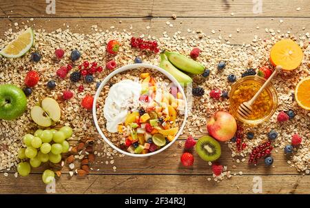 Dall'alto di deliziosi muesli in ciotola disposti su legno tavolo con farinata d'avena sparsa e frutti di bosco e frutti maturi assortiti Foto Stock