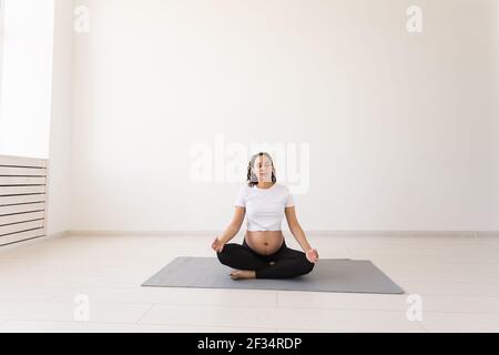 Bella donna in gravidanza sana medita prima della lezione di yoga e si rilassa mentre si siede sul tappetino sul pavimento. Concetto di preparazione fisica e mentale Foto Stock