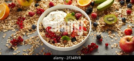 Da sopra ciotola di muesli naturali con frutta e yogurt posto vicino ingredienti assortiti sul tavolo la mattina Foto Stock