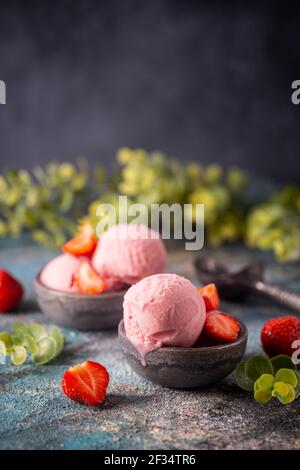 Gelato alla fragola in un recipiente con fragole fresche su sfondo blu Foto Stock