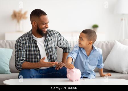 Padre e Figlio che mettono i soldi di risparmio personali in Piggybank Indoor Foto Stock