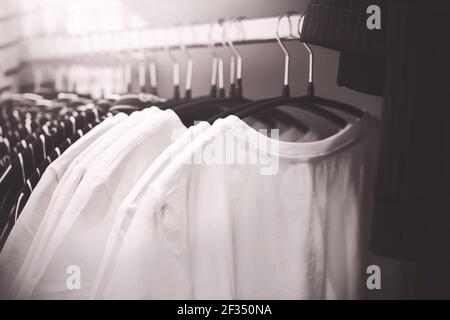 Un'immagine in bianco e nero di semplici T-shirt per uso quotidiano appese su appendiabiti nel guardaroba. Shopping in un negozio di abbigliamento. Cose eleganti. Foto Stock