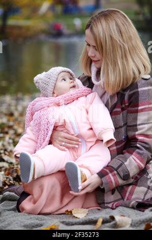 Bella bambina con madre seduta sulla plaid. Famiglia all'aperto. Adorabile bambina in abiti caldi al pic-nic in autunno parco il giorno di sole. Pret Foto Stock