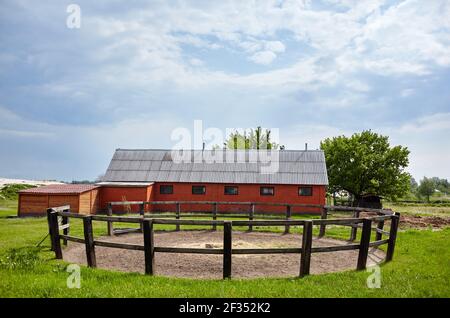 Cortale di legno per dressage cavallo contro un cielo blu in una giornata di sole. Paddock in erba su terreni agricoli con recinzione in legno. Vista rurale prato e recintato luogo fo Foto Stock