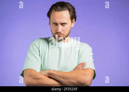 Uomo arrabbiato offeso che tiene le braccia incrociate e fissando la macchina fotografica con lo sguardo scettico e diffidente, ritenendosi pazzo a qualcuno. Espressioni facciali umane Foto Stock