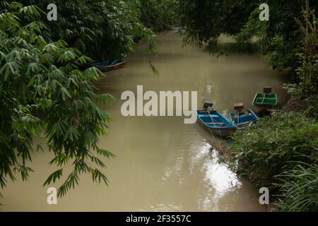 Un fiume verde marrone fiancheggiato da alberi tropicali della foresta pluviale a Gunung Kidul su Java, Indonesia con piccole barche a motore fisher, Foto Stock