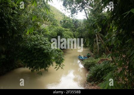 Un fiume verde marrone fiancheggiato da alberi tropicali della foresta pluviale a Gunung Kidul su Java, Indonesia con piccole barche a motore fisher, Foto Stock