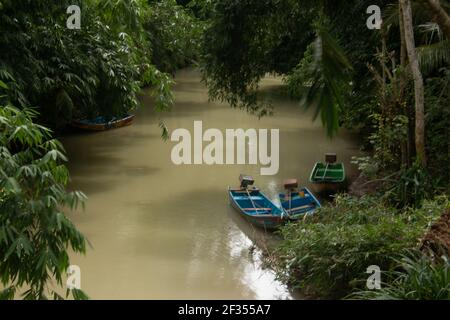 Un fiume verde marrone fiancheggiato da alberi tropicali della foresta pluviale a Gunung Kidul su Java, Indonesia con piccole barche a motore fisher, Foto Stock