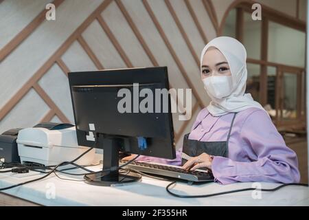 musulmana asiatica che lavora usando il pc mentre indossa il viso medico maschera Foto Stock