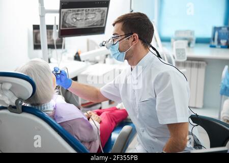 Dentista che sposta il trapano vicino alla bocca del pensionato Foto Stock