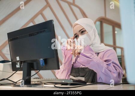 musulmana asiatica che lavora usando il pc mentre indossa il viso medico maschera Foto Stock