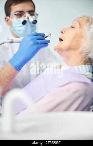 Dentista che fa un trattamento della signora anziana con il trapano Foto Stock