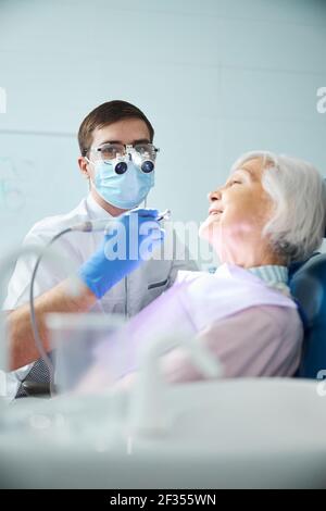 Medico qualificato che cerca di macchina fotografica con il trapano vicino donna felice Foto Stock