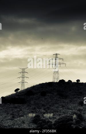 Silhouette di torri elettriche su una cima di una collina. Contro il cielo drammatico con le nuvole. Foto Stock