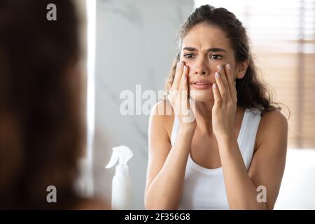 Donna infelice che guarda le rughe che toccano la pelle del viso in bagno Foto Stock