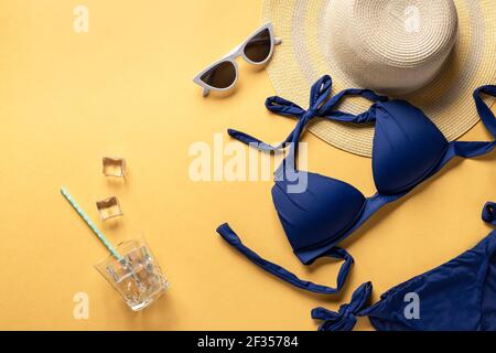 Tempo di divertimento estivo e accessori su sfondo giallo. Costume da bagno blu, cappello di paglia e occhiali da sole. Immagine orizzontale, posto per il testo Foto Stock
