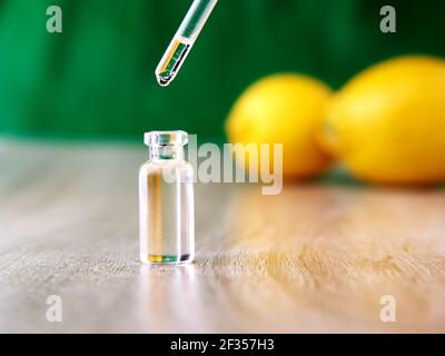 Una goccia di liquido gocciola in una fiala di vetro da una pipetta che si trova sopra di essa, sullo sfondo sono presenti due limoni e uno sfondo verde. Foto Stock