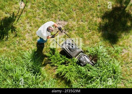 L'uomo si prende cura del prato. Vista dall'alto. Un uomo taglia il prato con un rasaerba Foto Stock