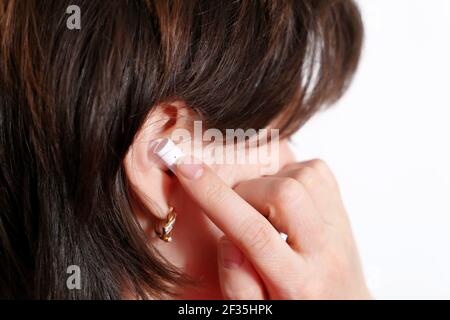 Donna che tocca l'auricolare wireless nell'orecchio. Cuffie, ascolto di musica e concetto di chiamata vocale Foto Stock