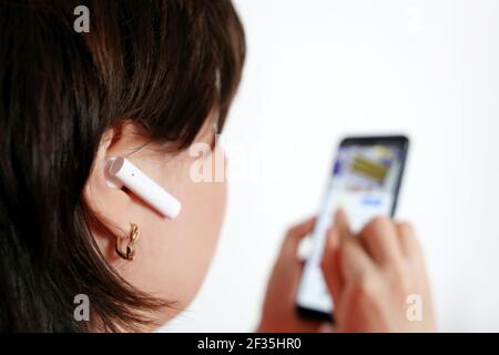 Donna con auricolare wireless nell'orecchio. Cuffie, ascolto di musica e visione di video Foto Stock