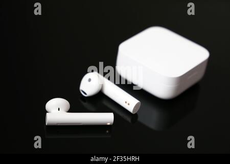 Auricolari wireless con custodia di ricarica bianca su un tavolo in vetro nero. Cuffia per l'ascolto di musica e chiamate vocali Foto Stock