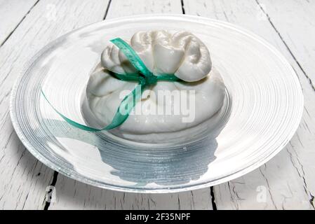 Burrata di mozzarella, formaggio Apulia stretriato ripieno di panna in un piatto di vetro su una superficie di legno di colore bianco Foto Stock