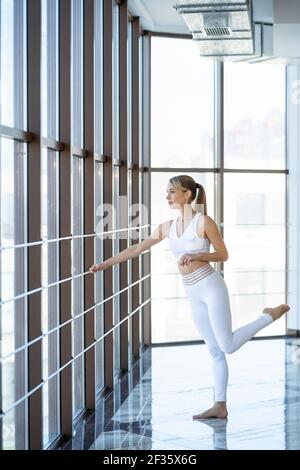 Bella donna in abbigliamento sportivo bianco in sala ginnastica. Ragazza atletica che si riscalda prima di formazione Foto Stock