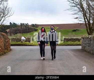 East Lothian, Scozia, Regno Unito, 15 marzo 2021. I bambini della scuola ritornano alla scuola secondaria: Gemelli, Louisa e Imogen, di 12 anni e in S1 sono tornati oggi per la prima volta al North Berwick High School dal recente blocco durante la pandemia del coronavirus, ma solo per 3 ore oggi per tutta la settimana, quando si scende dal bus scolastico a Kilduff Foto Stock
